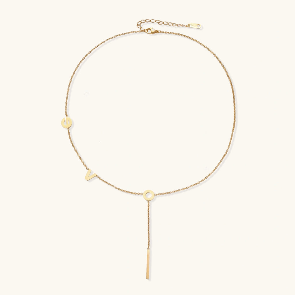 Gold Y-shaped necklace with L-O-V-E letter charms and vertical bar pendant on delicate chain against cream background