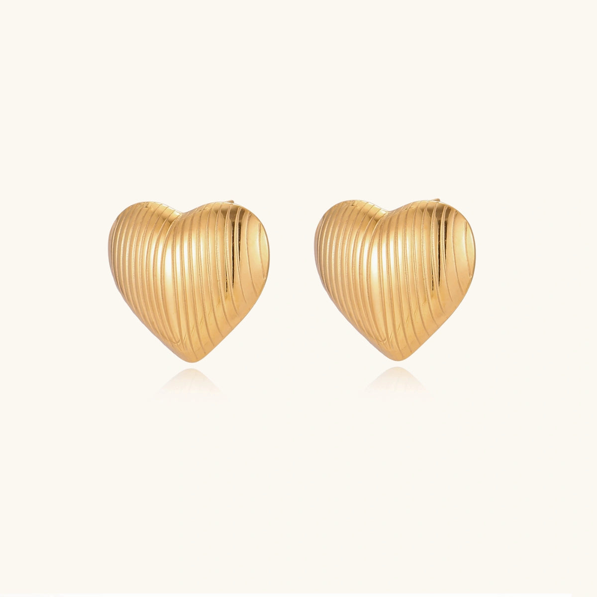 Gold heart-shaped stud earrings with parallel ridged texture on cream background