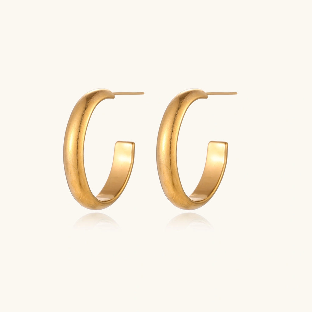 Chunky tubular hoop earrings in warm 14K gold-plated finish with smooth polished surface on cream background.
